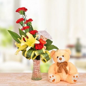 Floral Arrangement of 8 Red Carnations, 2 Yellow Asiatic Lilies and a 3 Inches Brown Teddy Bear with dracaena leaves in a Glass Vase with 1 Brown Teddy Bear (12 Inches)